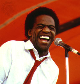 Al Green in front of a microphone (in a red tie) with a huge smile.