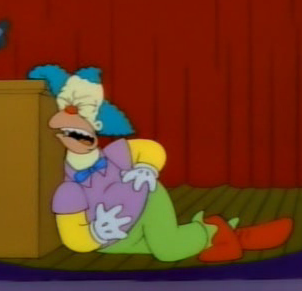 Krusty gripping his stomach, having fallen over by his podium