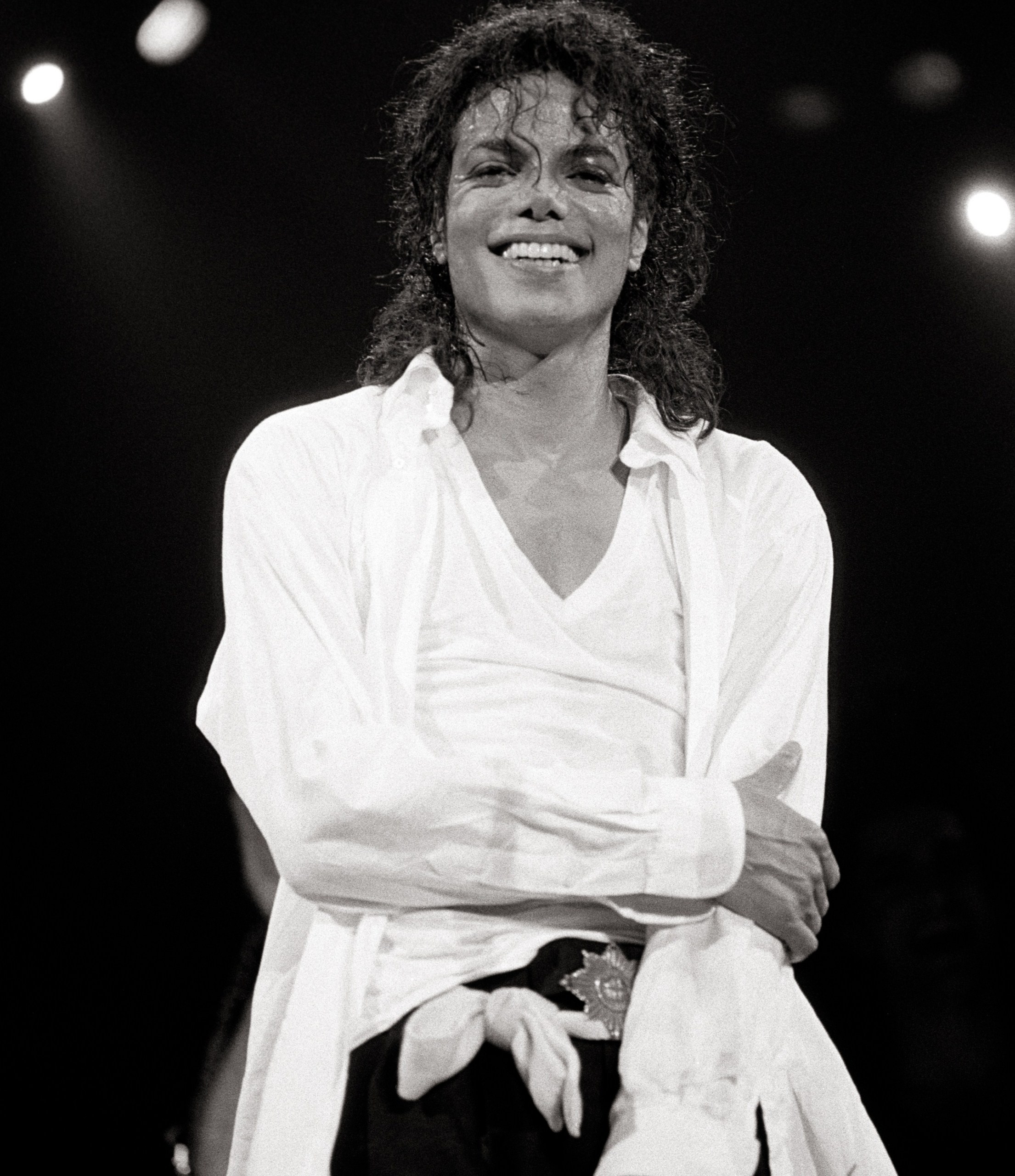 Michael Jackson smiling on stage, lightly holding arm during the Bad tour
