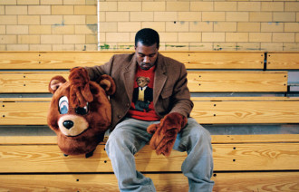 Kanye West sitting in college bleachers in mascot costume without the bear head on