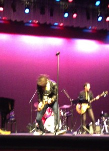 Eric McCormack whipping his hair while playing the tennis racket as a guitar at his concert.