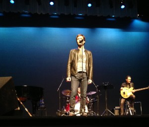 Eric McCormack in front of band and blue backdrop at the mic, singing a ballad during "The Concert I Never Gave" at the El Portal Theatre Los Angeles