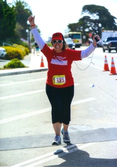 Aurora running in a red shirt with her hands up on a fairly empty street at Run Montecito-Summerland