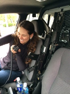 Aurora laughing with a walkie talkie in a police cruiser