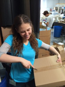 Aurora De Lucia looking down and smiling while opening a box at Trash for Teaching