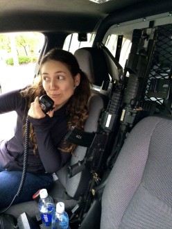 Aurora De Lucia in a police cruiser pretending to talk on a walkie talkie