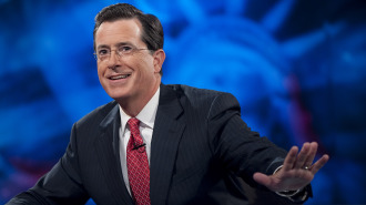 Stephen Colbert on his show, sitting at his desk with the Statue of Liberty in the background