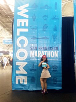 Aurora standing with her bib in front of a sign at the San Francisco Marathon expo